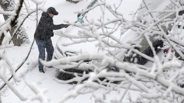 Мужчина убирает снег с лобового стекла своего автомобиля во дворе жилого дома в Москве